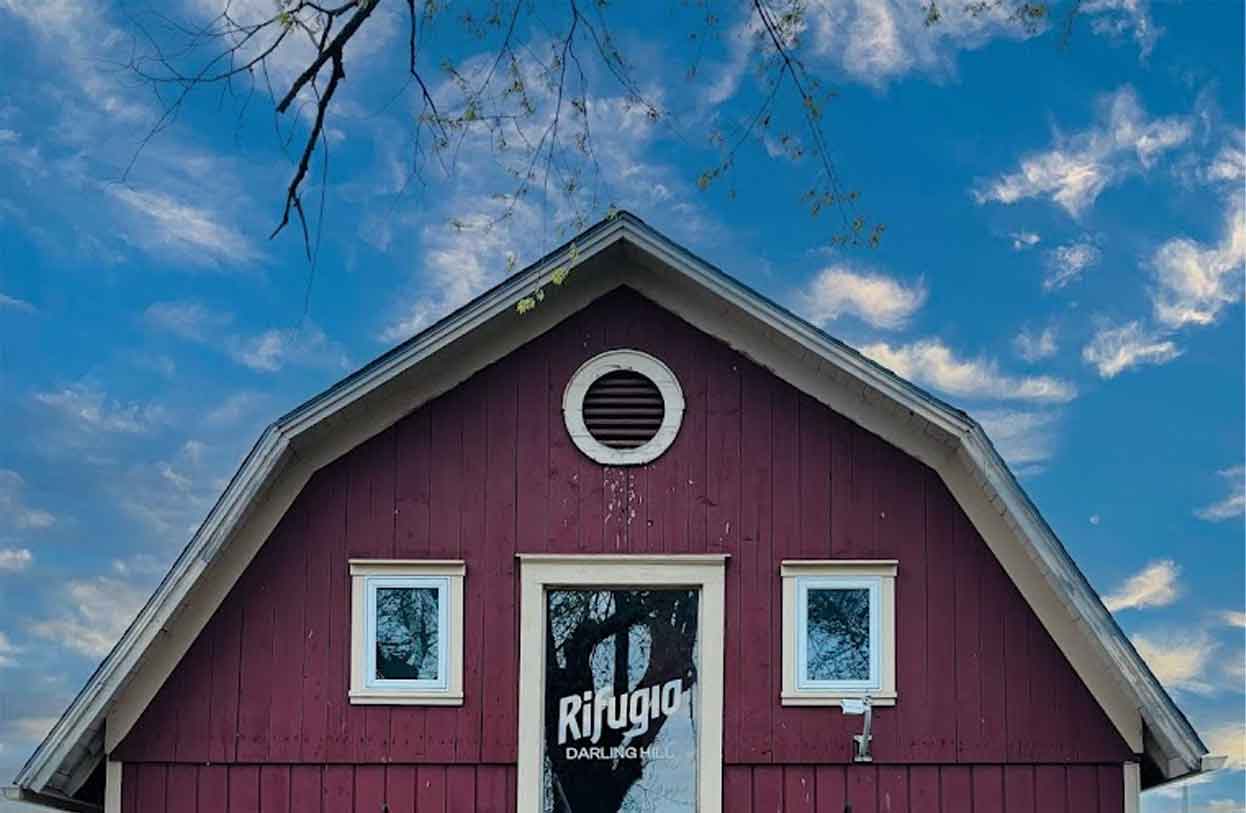 The deep-red Rifugio Darling Hill barn with the Rifugio script wordmark on the front door, framed by a clear blue sky