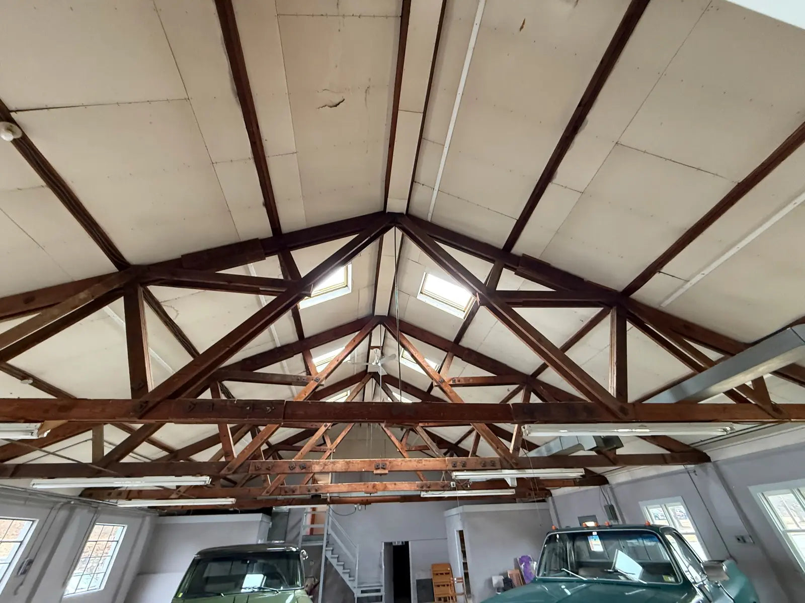 The vaulted ceiling&rsquo;s exposed wood roof trusses and skylights, with two vintage pickup trucks parked in the bay below