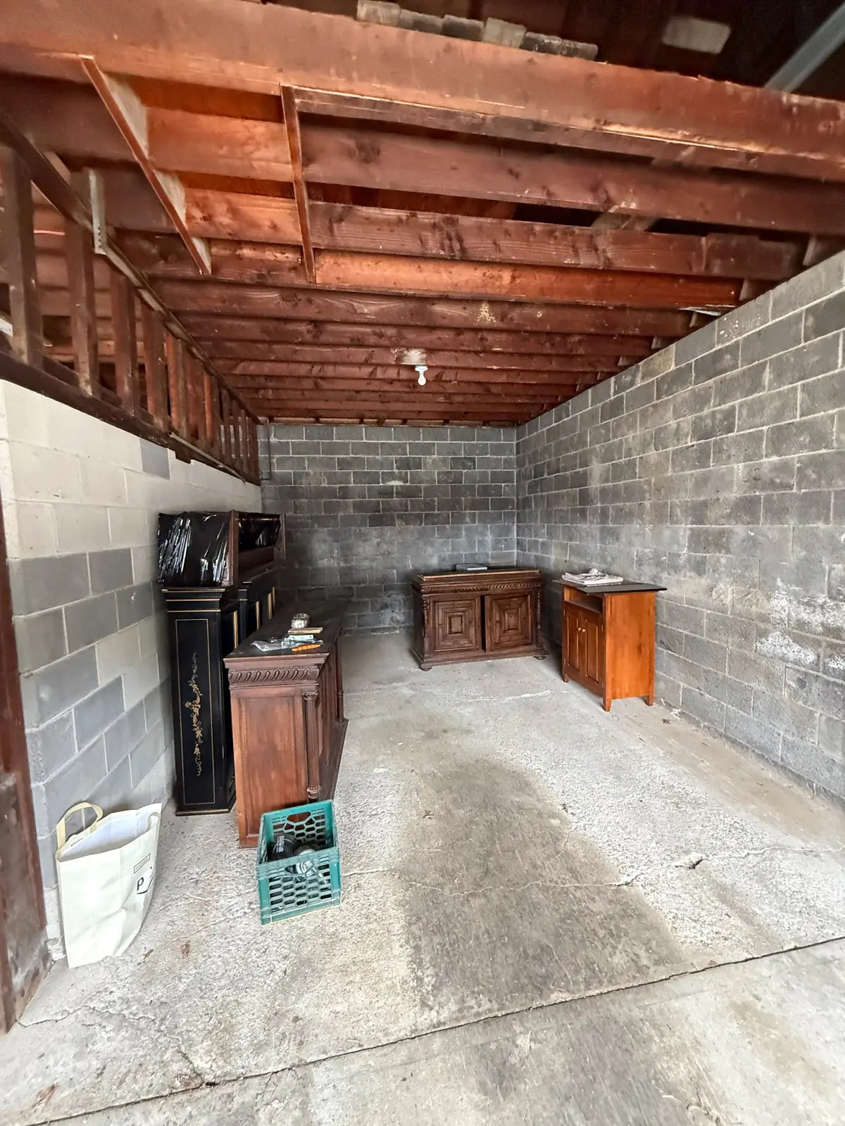 Another storage bay under the same rough wood ceiling, stacked with old cabinets and furniture waiting to be cleared out